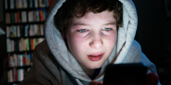 Junge, der mit verweinten Augen auf den Bildschirm seines Laptops schaut