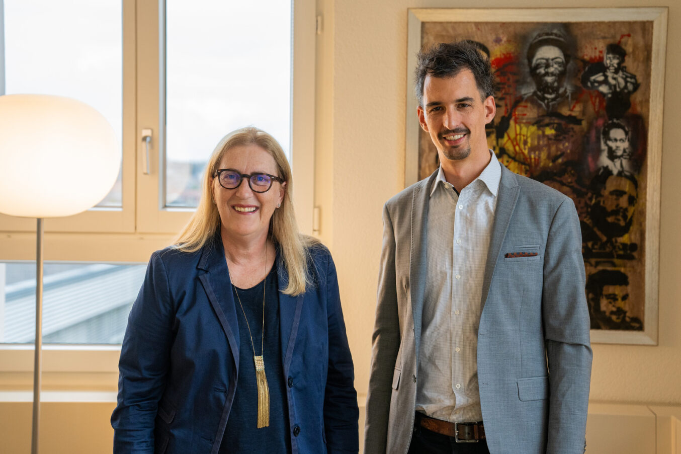 Frau und Mann posieren für ein Foto in einem Büro mit einem Kunstgemälde im Hintergrund