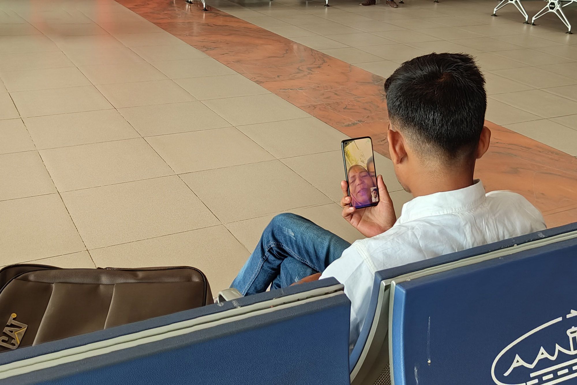 chicos sentado en el interior de un aeropuerto haciendo una videollamada por el móvil