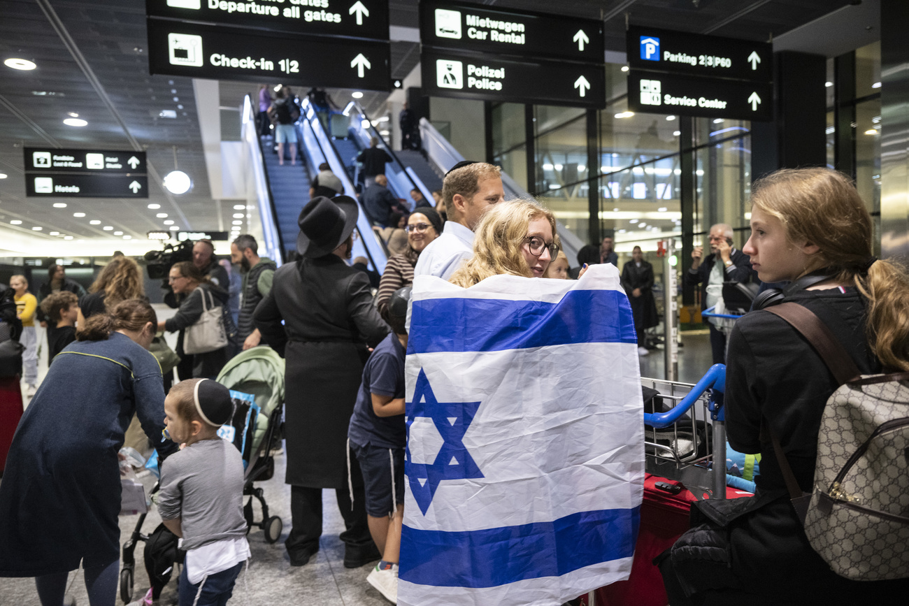 persone nella hall di un aeroporto con bandiera israeliana