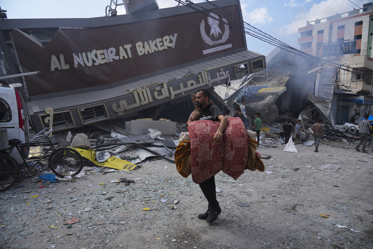 Man with mattress walks past a ruined bakery