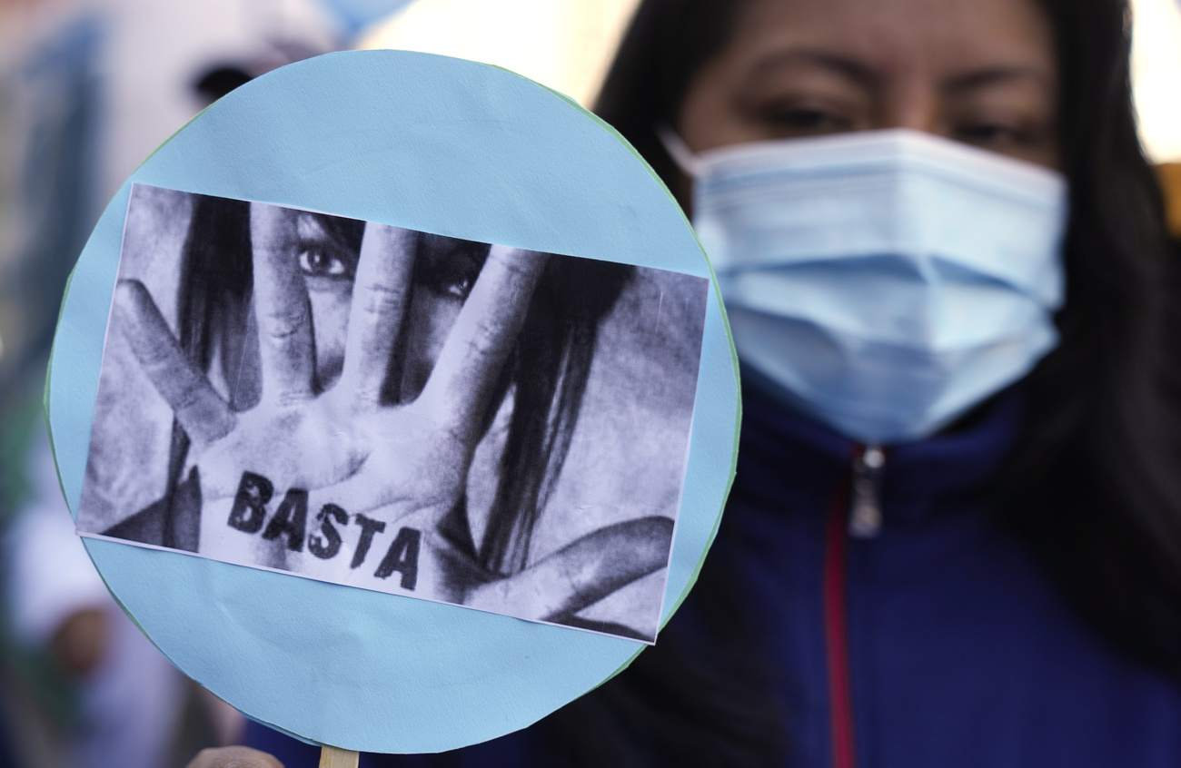 donna con maschera chirurgica mostra foto con donna che si copre il viso con una mano sulal quale c è la scritta BASTA