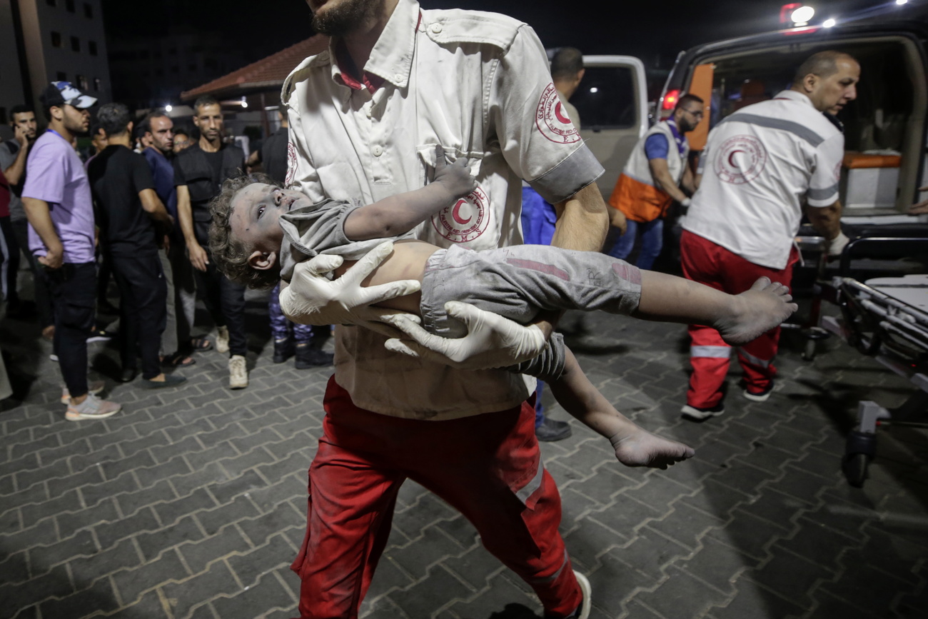 أحد العاملين في جمعية الهلال الأحمر الفلسطيني يحمل طفلاً جريحًا إلى مستشفى الشفاء في مدينة غزة.
