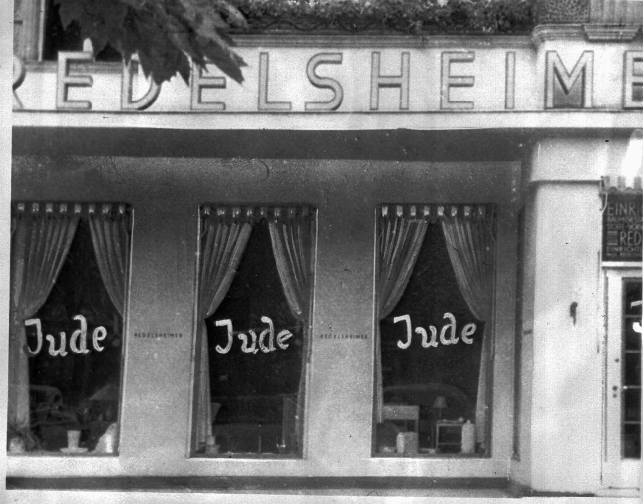 altes Foto mit Schaufenstern eines Geschäfts mit aufgeschmiertem Schriftzug Jude