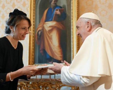 Eine Frau überreicht dem Papst in feierlicher Haltung ein Dokument