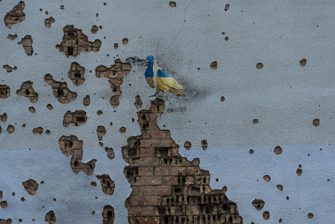 Eine zerschossene Wand mit einem gemalten Vogel in den ukrainischen Nationalfarben