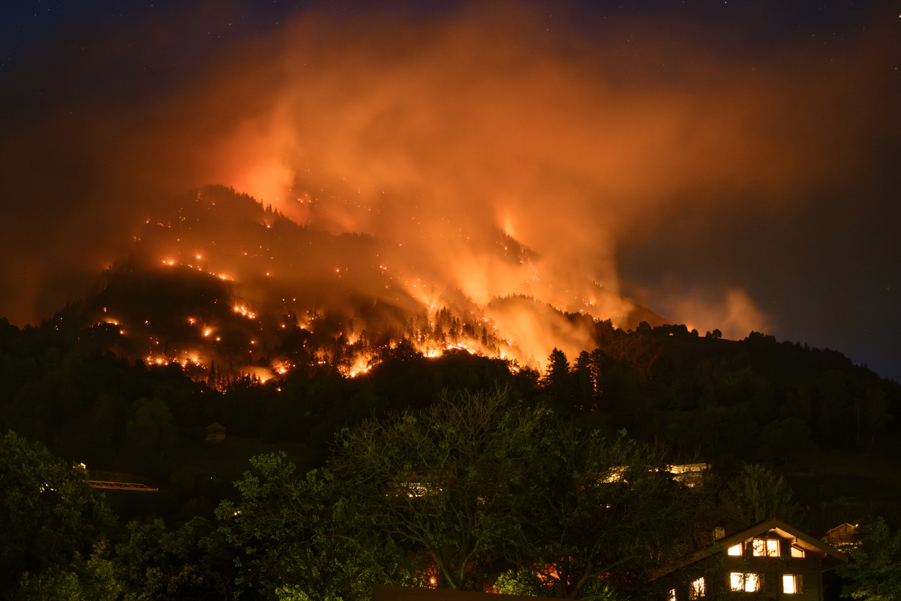 Brennender Wald, bei Nacht fotografiert, unten dem Berg ein Haus, in dem Licht brennt