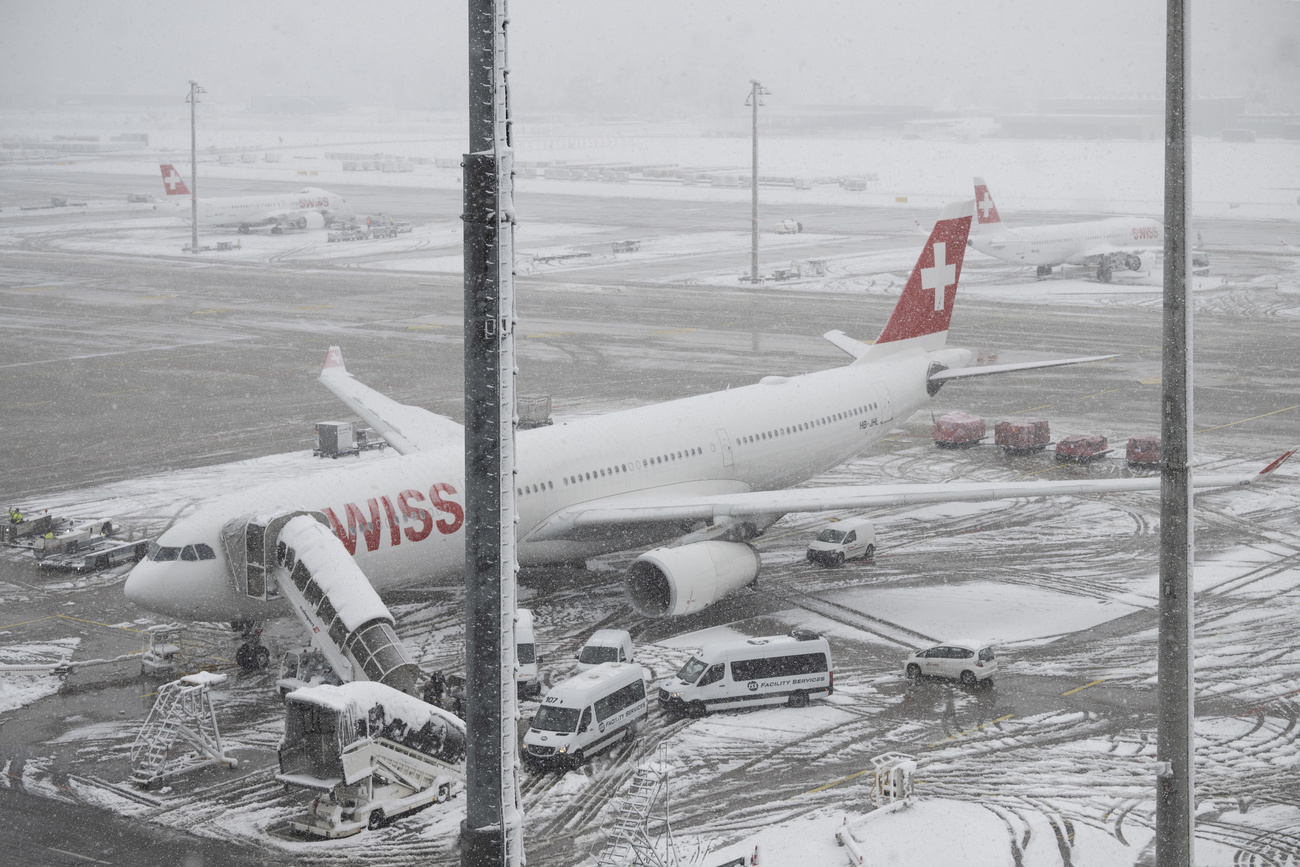 Eine schneebedeckte Maschine der Swiss, im Hintergrund das Flughafengelände im Schneetreiben