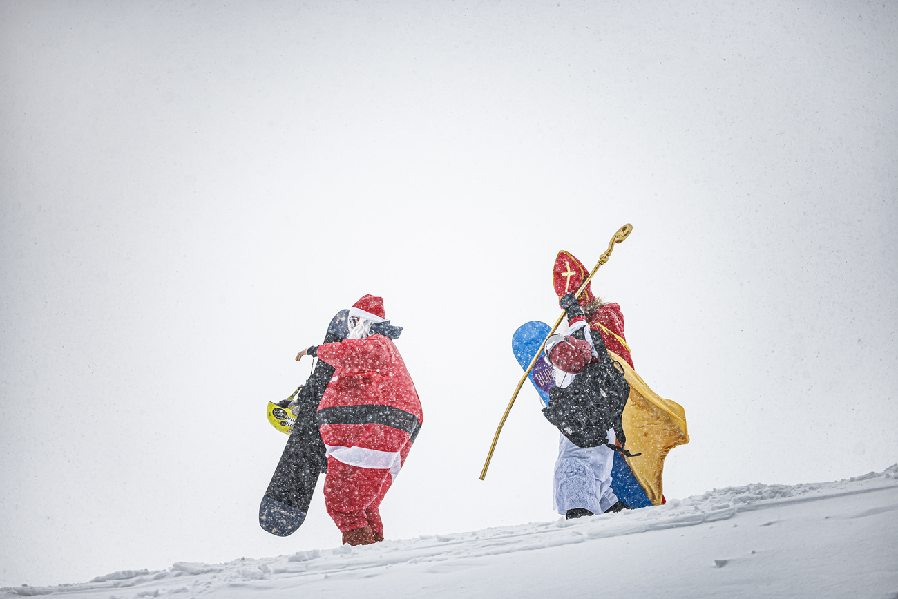 Ein Weihnachtsmann und ein Nikolaus mit Snowboard laufen durch den Schnee