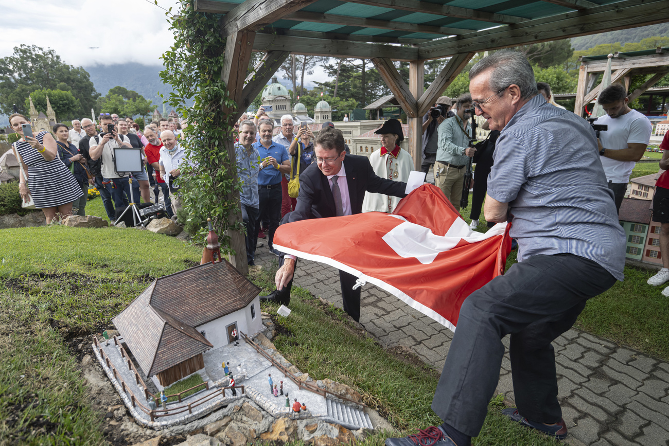 Vor viel Publikum zieht Albert Rösti eine Schweizer Flagge von der neuen Attraktion des Themenparks in Melide