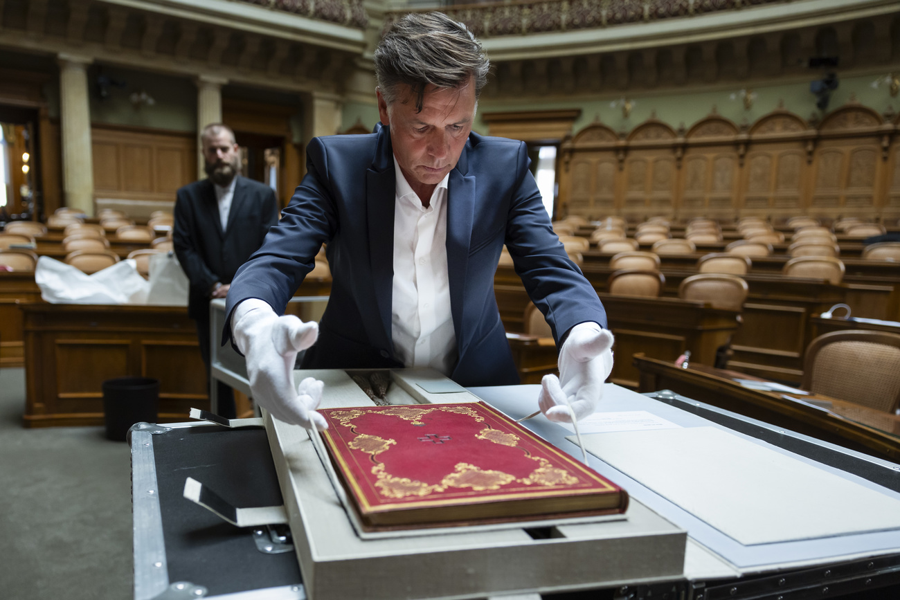 Restaurator Joel Aeby, mit weissen Handschuhen in einem leeren Saal, hantiert mit der Bundesverfassung.