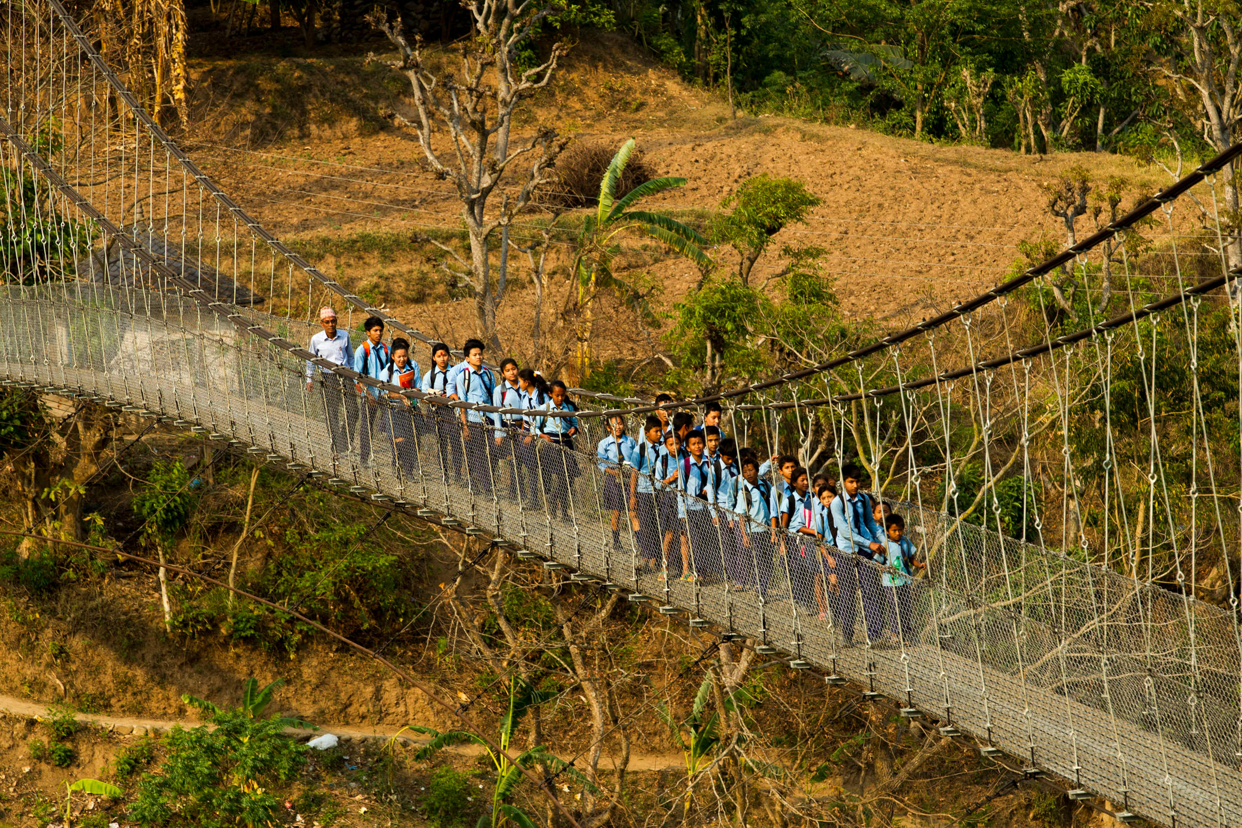 Schulkinder in Uniform auf einer Hängebrücke in Nepal