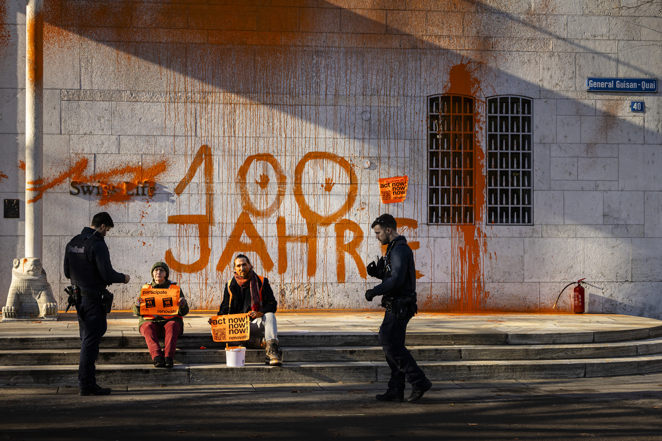Eine Aktivistin und ein Aktivist sitzen auf der Treppe vor dem mit oranger Farbe attakierten Hauptsitz von Swiss Life in Zürich