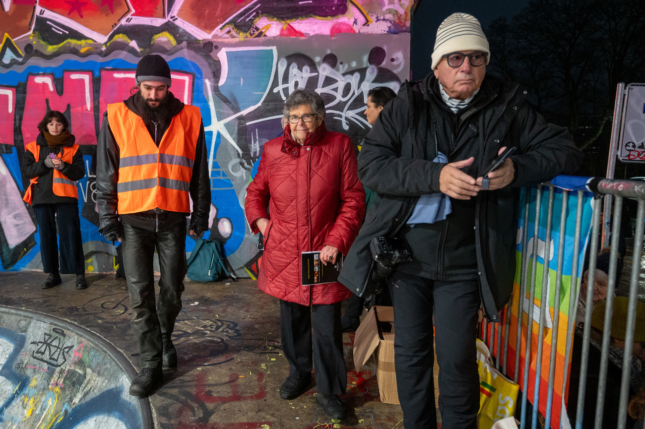 Ruth Dreyfuss und Personen in Leuchtwesten stehen vor einer Graffiti-Mauer