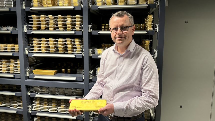 Mann in Goldtresor mit einem Goldbarren in den Händen