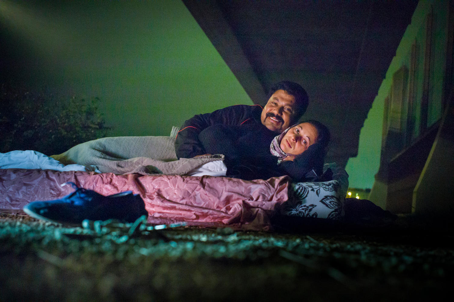 Two people sleeping under a bridge