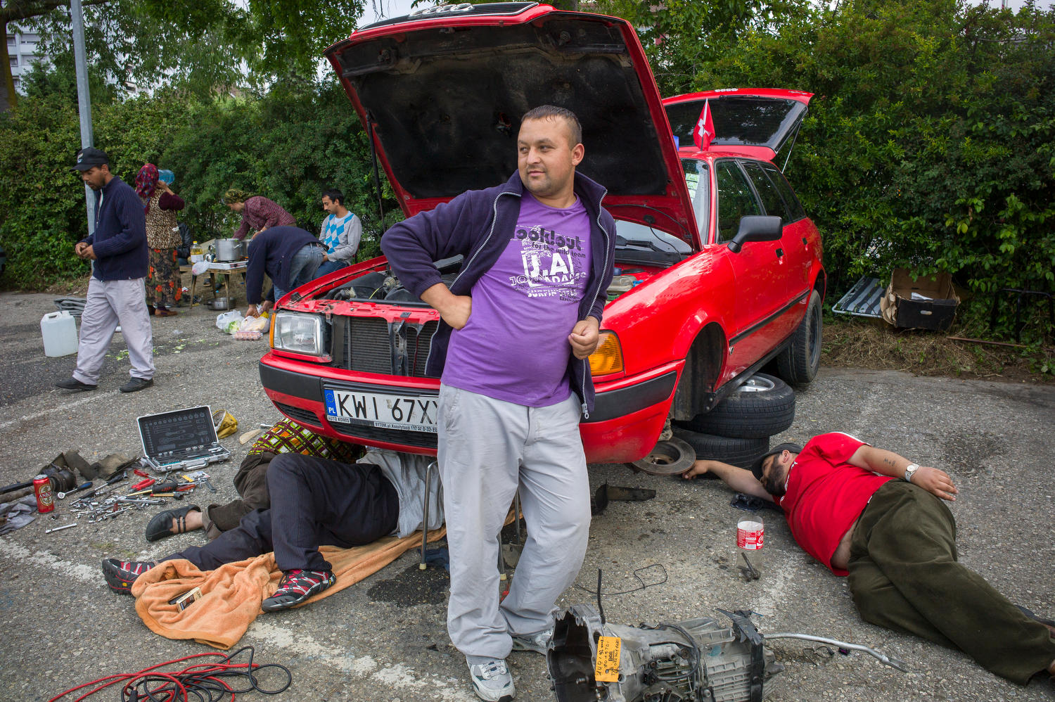 Un hombre apoyado en un coche que están arreglando