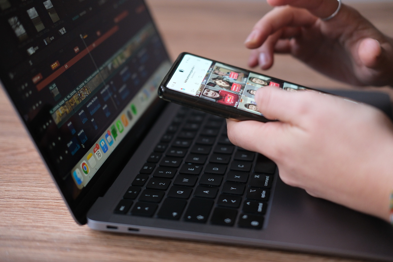Hände tippen am Smartphone, dahinter ein Laptop