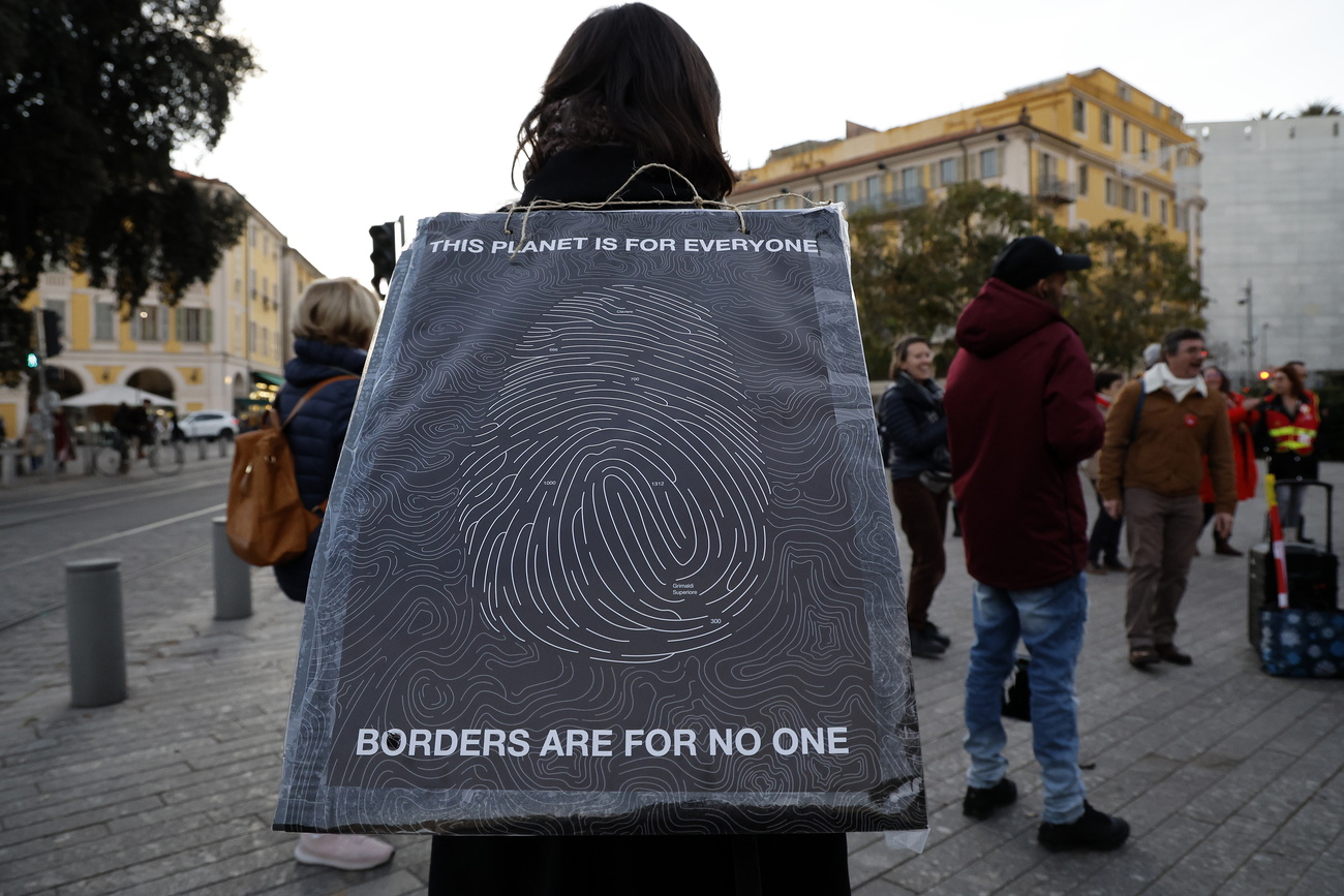 persona indossa cartello con scritta in inglese: questo pianeta è per tutti, le frontiere non sono per nessuno