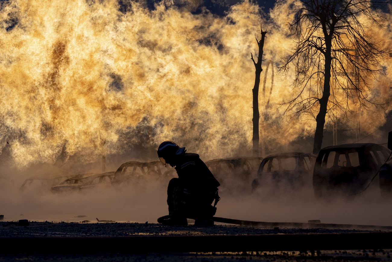 Feuerwehrmann bückt sich, hinter ihm tobt das Feuer.
