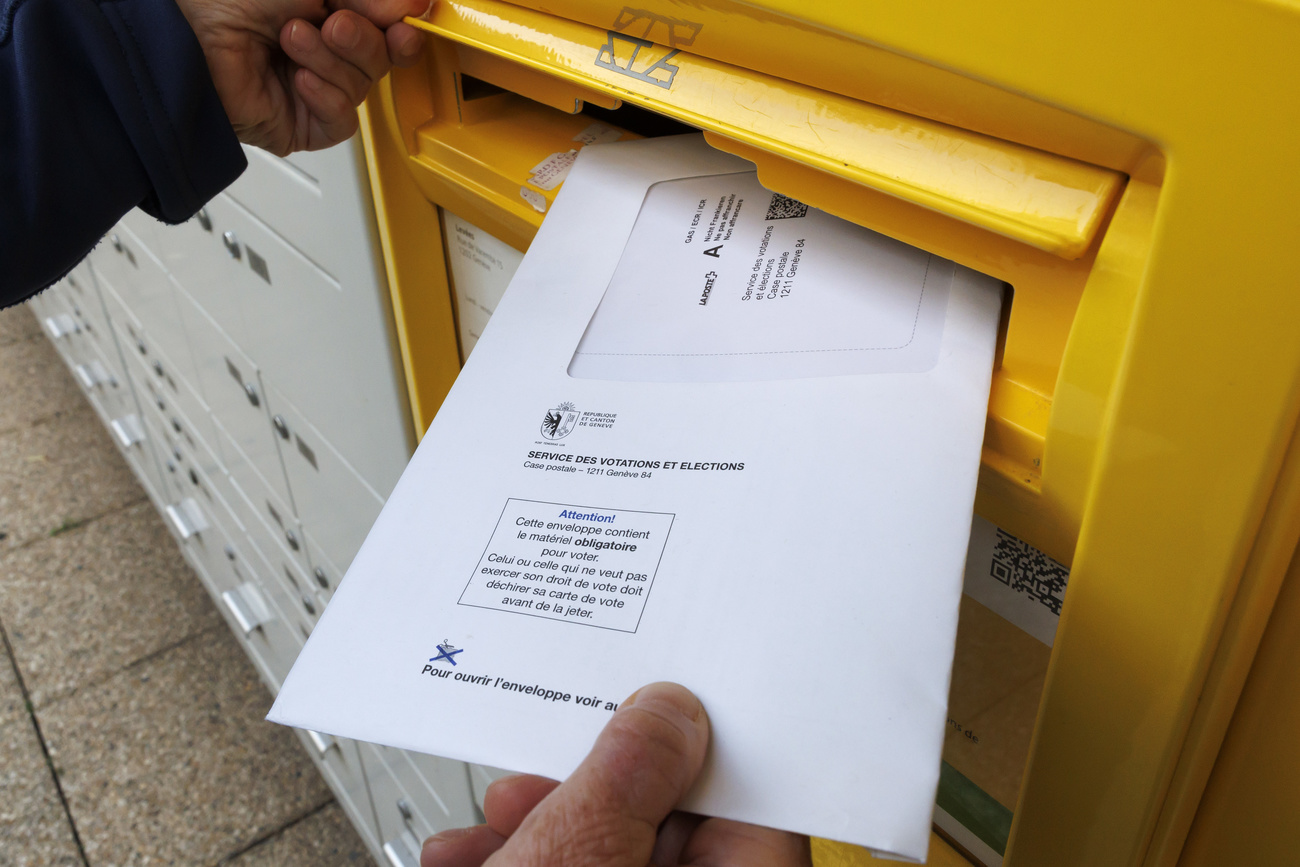 Hand, die ein Wahlcouvert in einen gelben Briefkasten der Schweizer Post einwirft