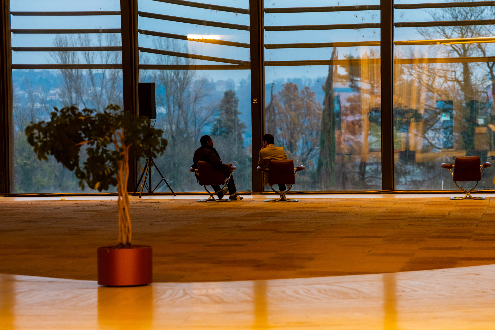 建物E棟の薄暗いロビーで、冬のパノラマ景色を眺める2人の職員