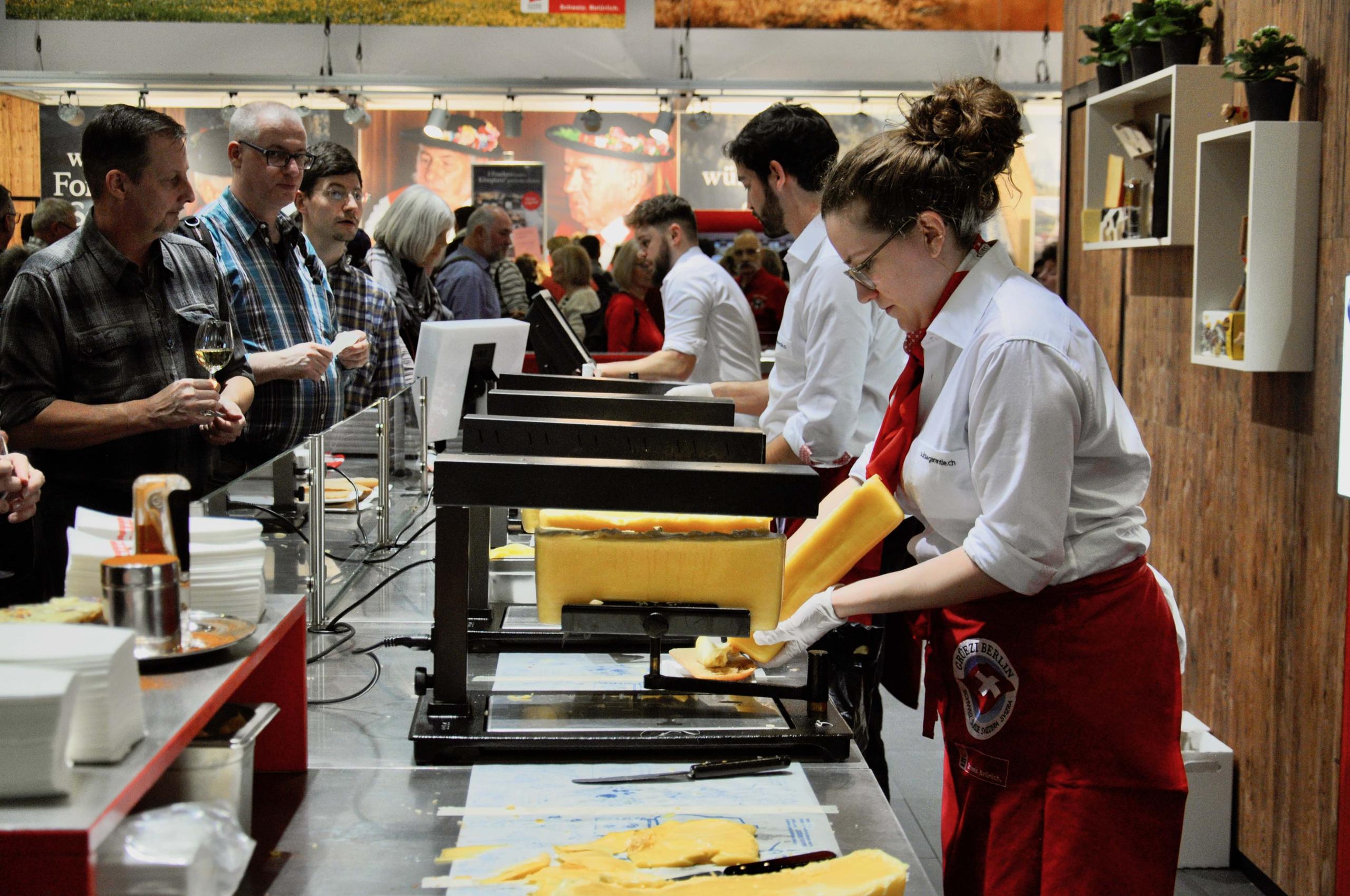 An einem langen Tisch wird Käse geschmolzen und auf Brötchen geschüttet.