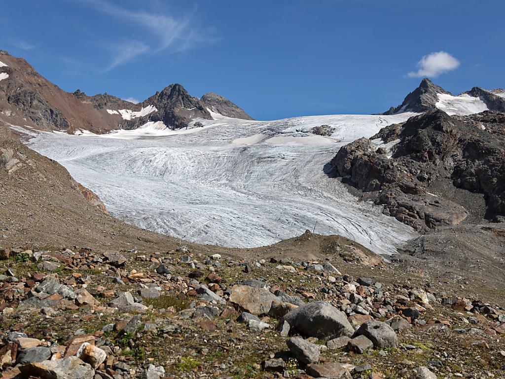 Bild eines Gletschers umgeben von Gestein und blauem Himmel.