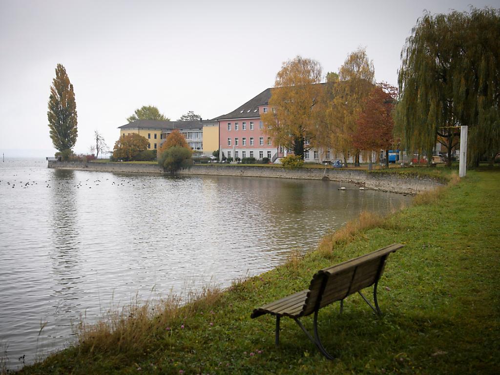 Bild einer Bank am Seeufer, im Hintergrund ein Haus.