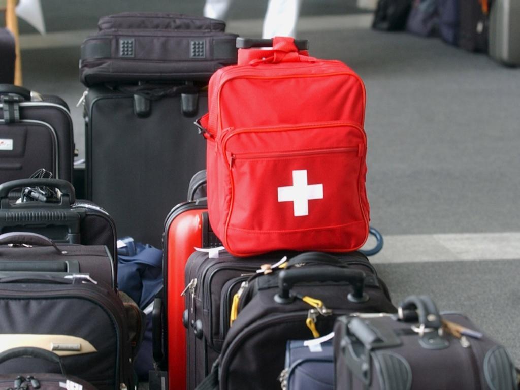 Ein roter Rucksack mit einem weissen Kreuz steht auf einer schwarzen Koffer.