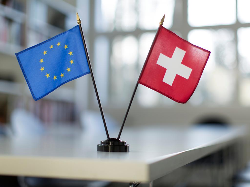 Eine Schweizer Fahne und eine Fahne der EU stehen auf einem Tisch.