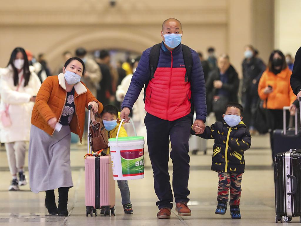 Eine chinesische Familie mit Koffern und Mundschutz in einer Halle.