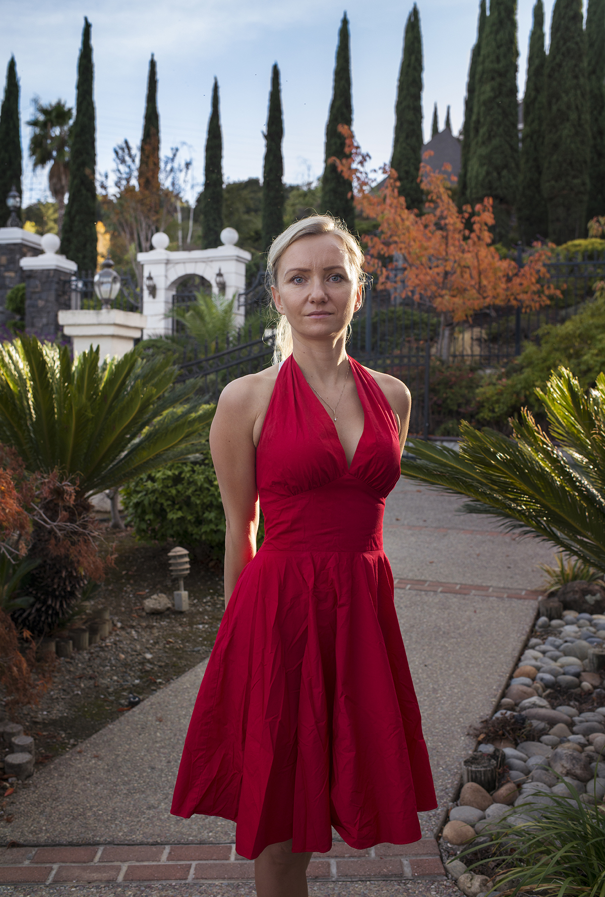 A person wearing a red dress stands looking to the camera.