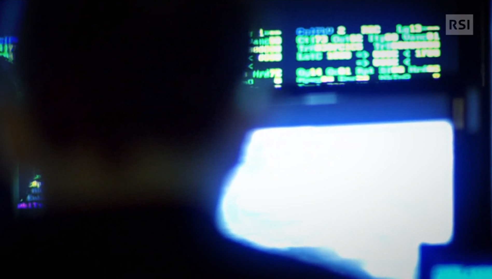 Di schiena, in controluce, uomo davanti a schermi del computer inserisce codici