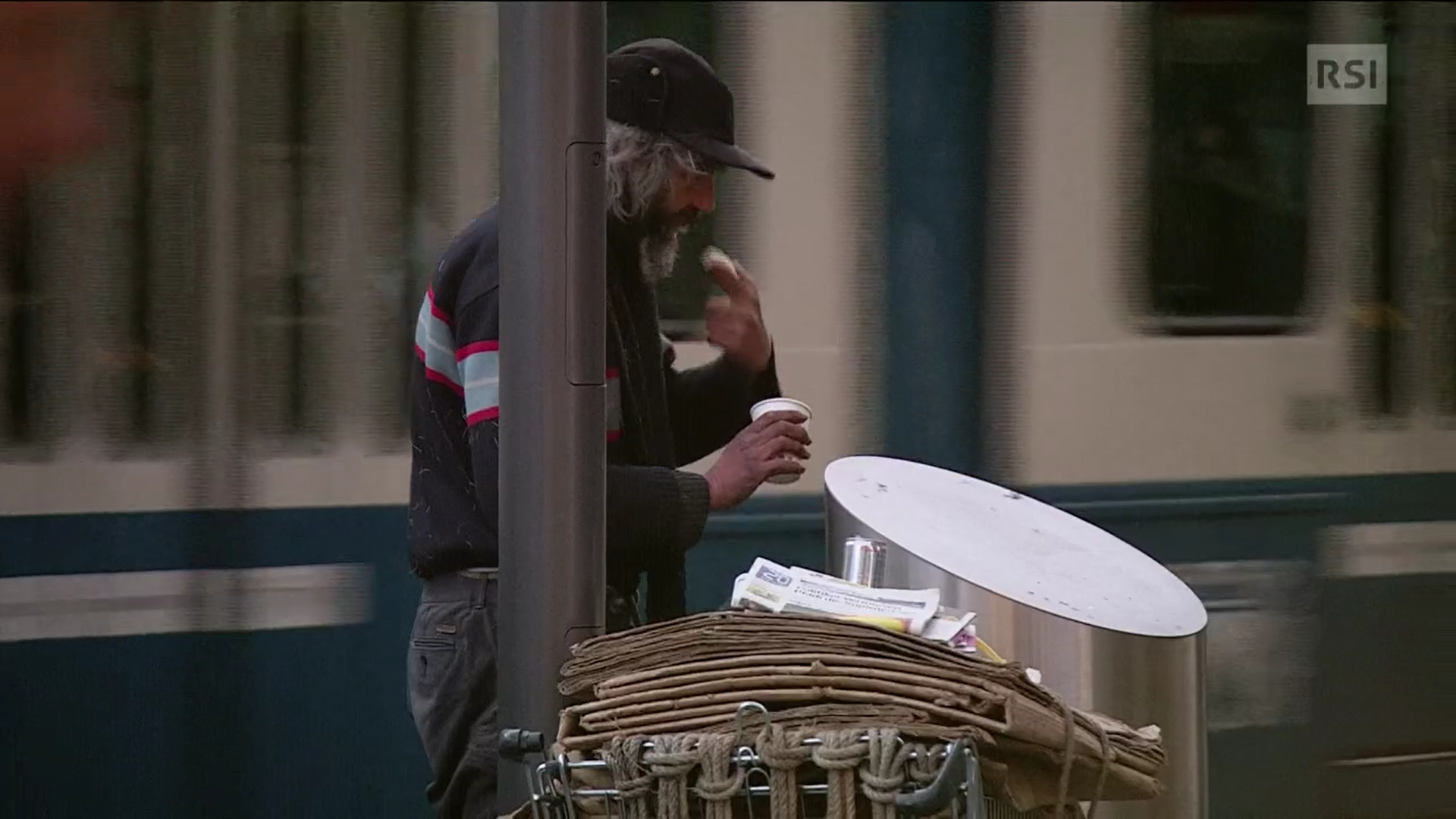 Uomo con berretto preleva da un cestino della spazzatura un alimento non completamente consumato.