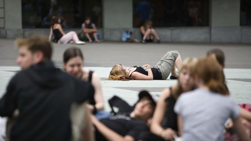 Junge Leute sitzen und liegen auf einem asphaltierten Platz