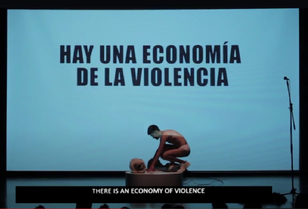 Un hombre desnudo y en cuclillas bajo un cartel con la leyenda: Hay una economía de la violencia.