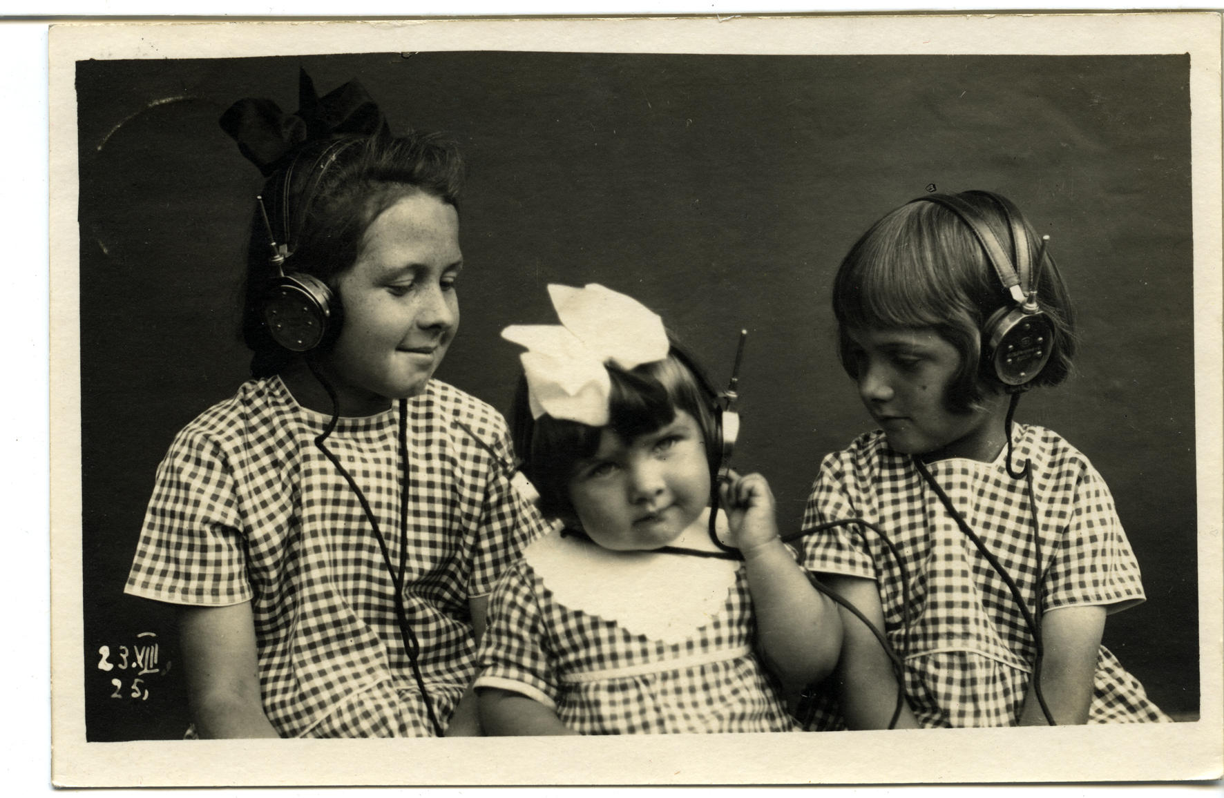 Drei Mädchen in gleichen Kleidchen hören Radio mit Kopfhörern, schwarz-weiss-Fotografie