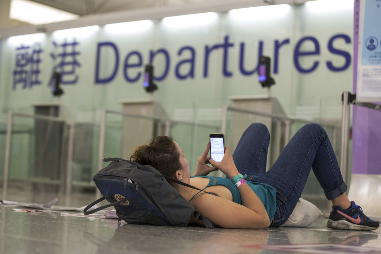 Eine Frau, die in einem asiatischen Flughafen auf dem Boden ruht, schaut auf ihr Smartphone