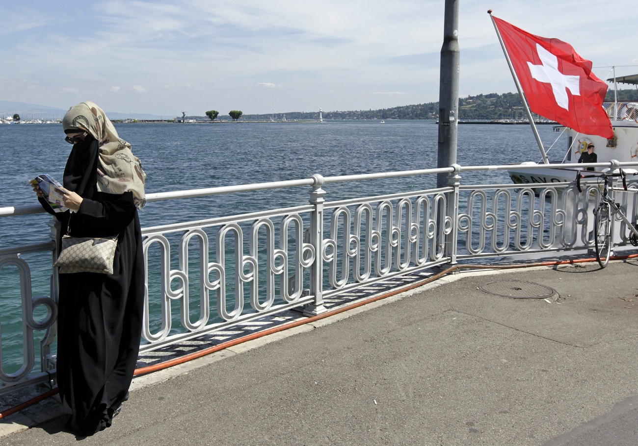 une femme voilée à côté d un drapeau suisse
