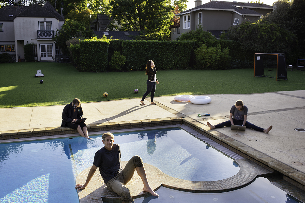 Four people working on devices. They are standing and sitting around a swimming pool.