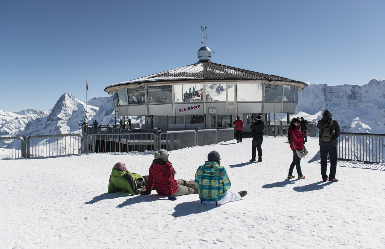 Touristen liegen auf dem Schilthorn vor dem Drehrestaurant in der Sonne, dahinter die Bergkulisse