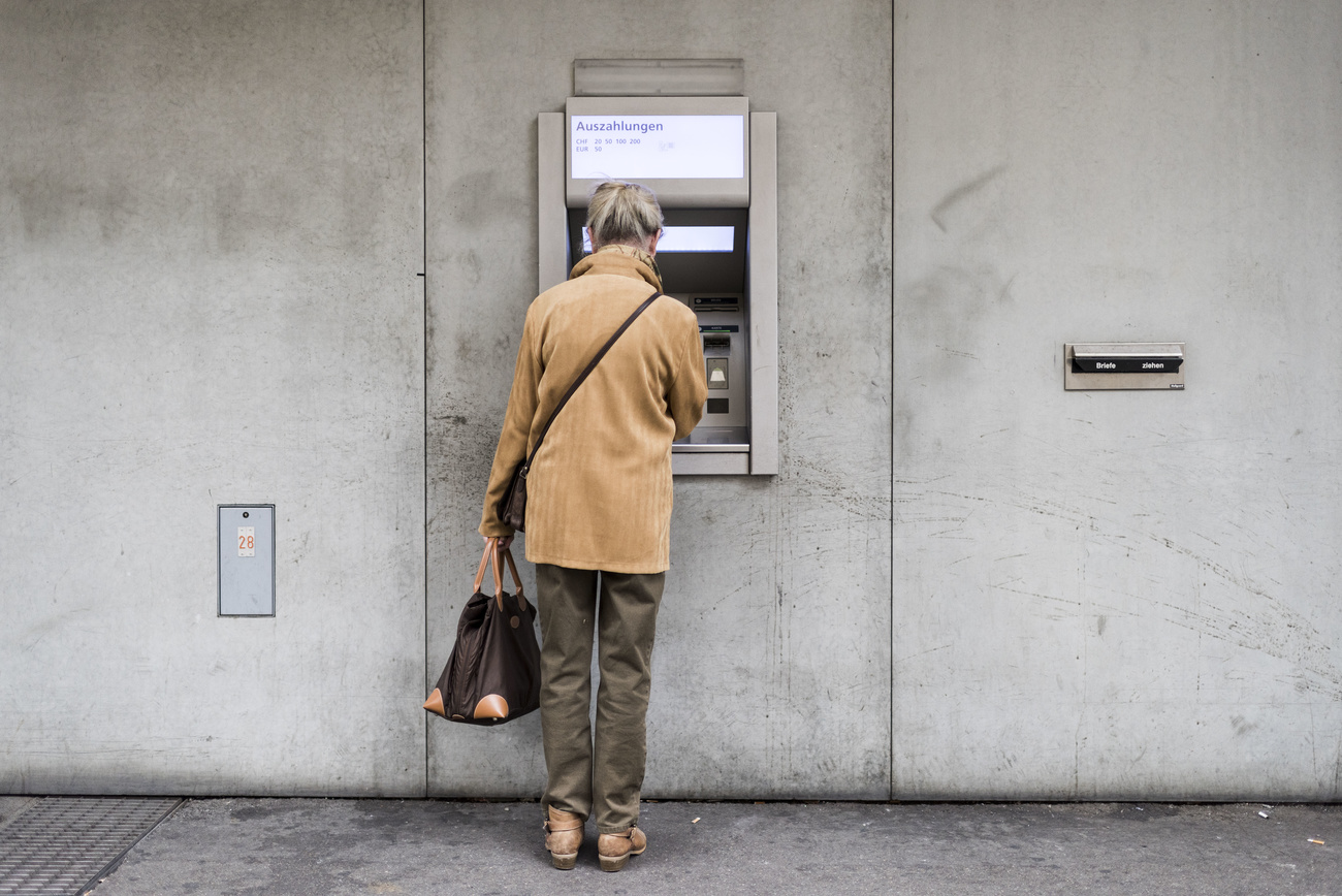 Eine ältere Frau steht vor dem Bankautomaten und will Geld abheben.