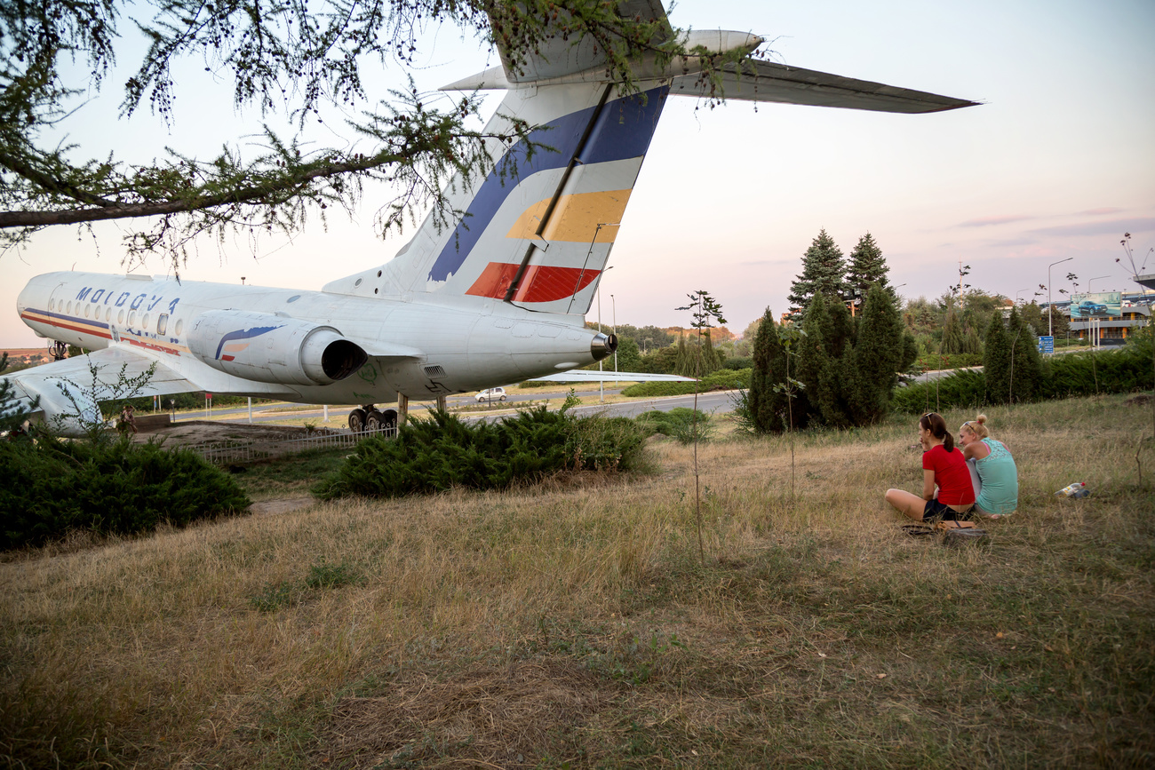 two women sitting on grass looking at an airplane
