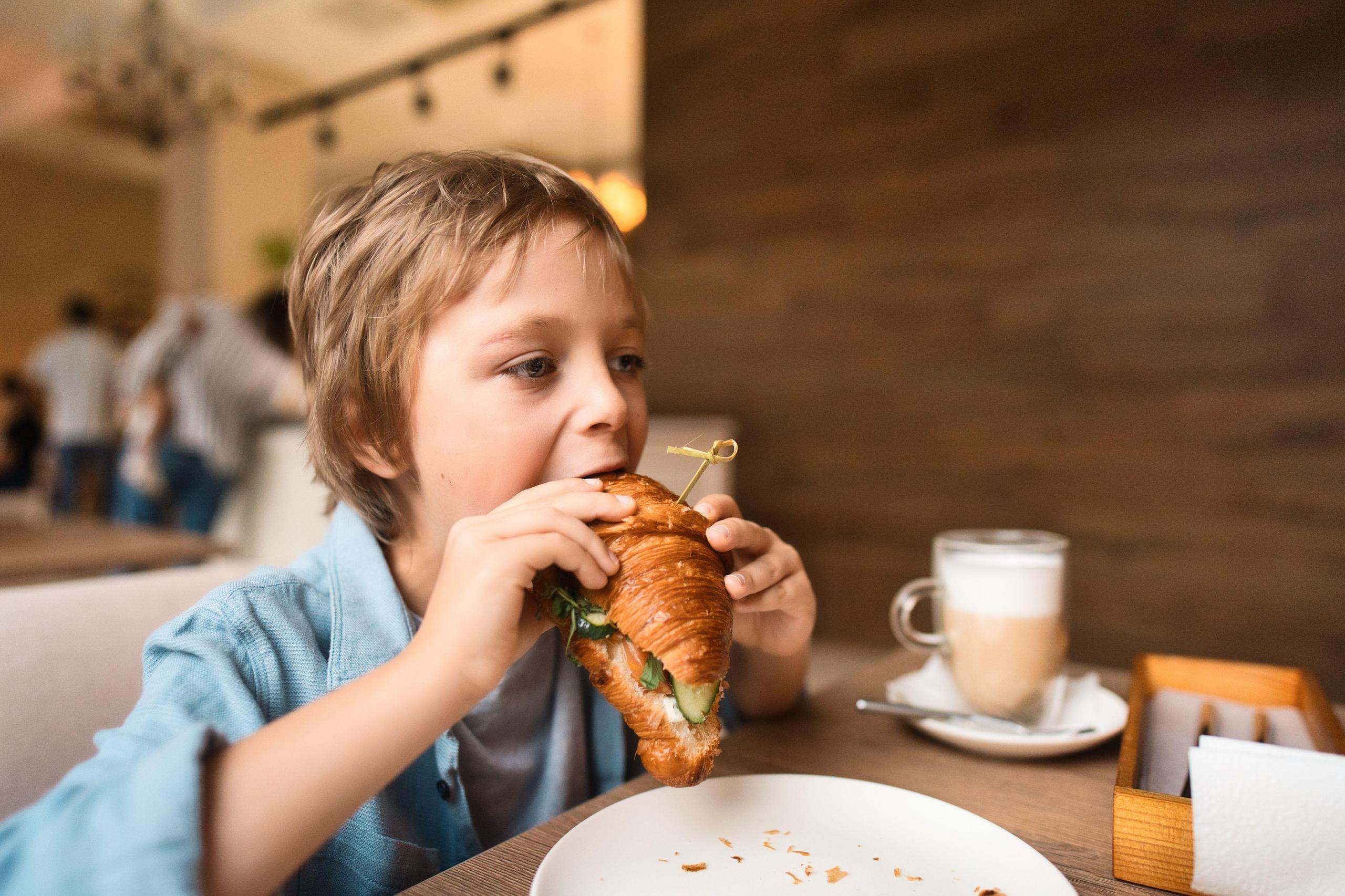 Kleiner Junge isst ein Croissant-Sandwich