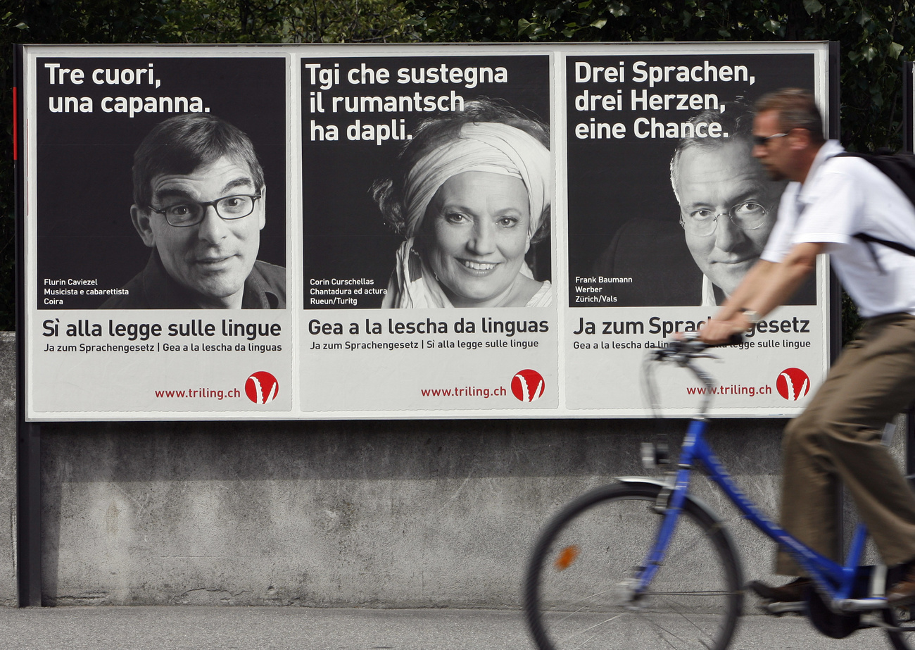 ciclista passa davanti a tre manifesti in tre lingue diverse