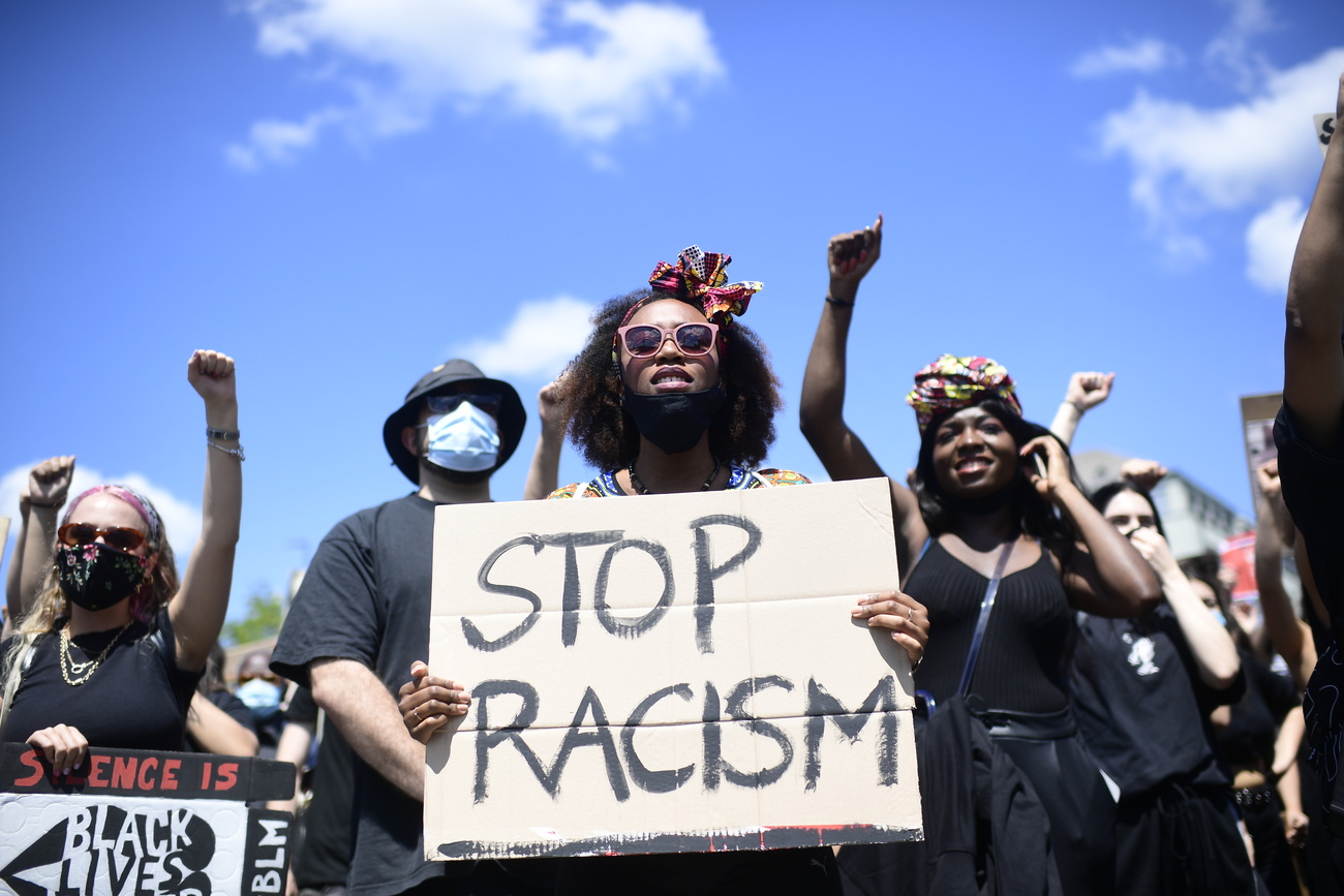 Photo of a woman holding a sign saying "No racism"