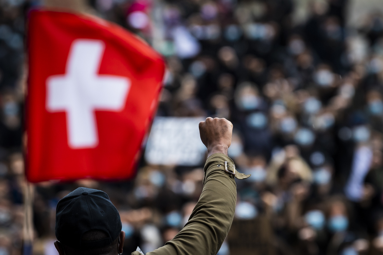 Photo of a crowd and Swiss flag in the background and black man
