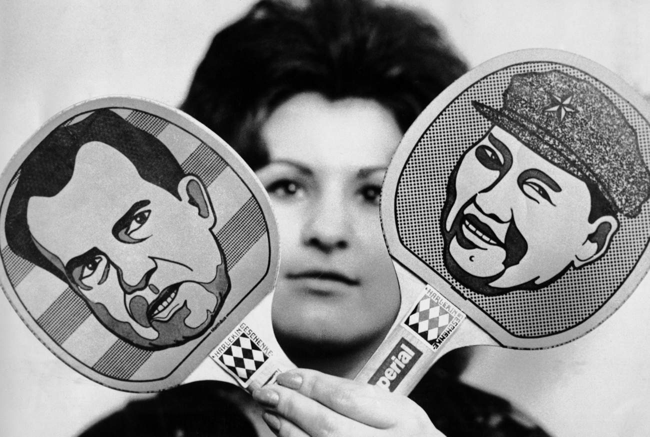 Frau hält zwei Ping Pongschläger hoch, einer zeigt Nixon, einer Mao Zedong