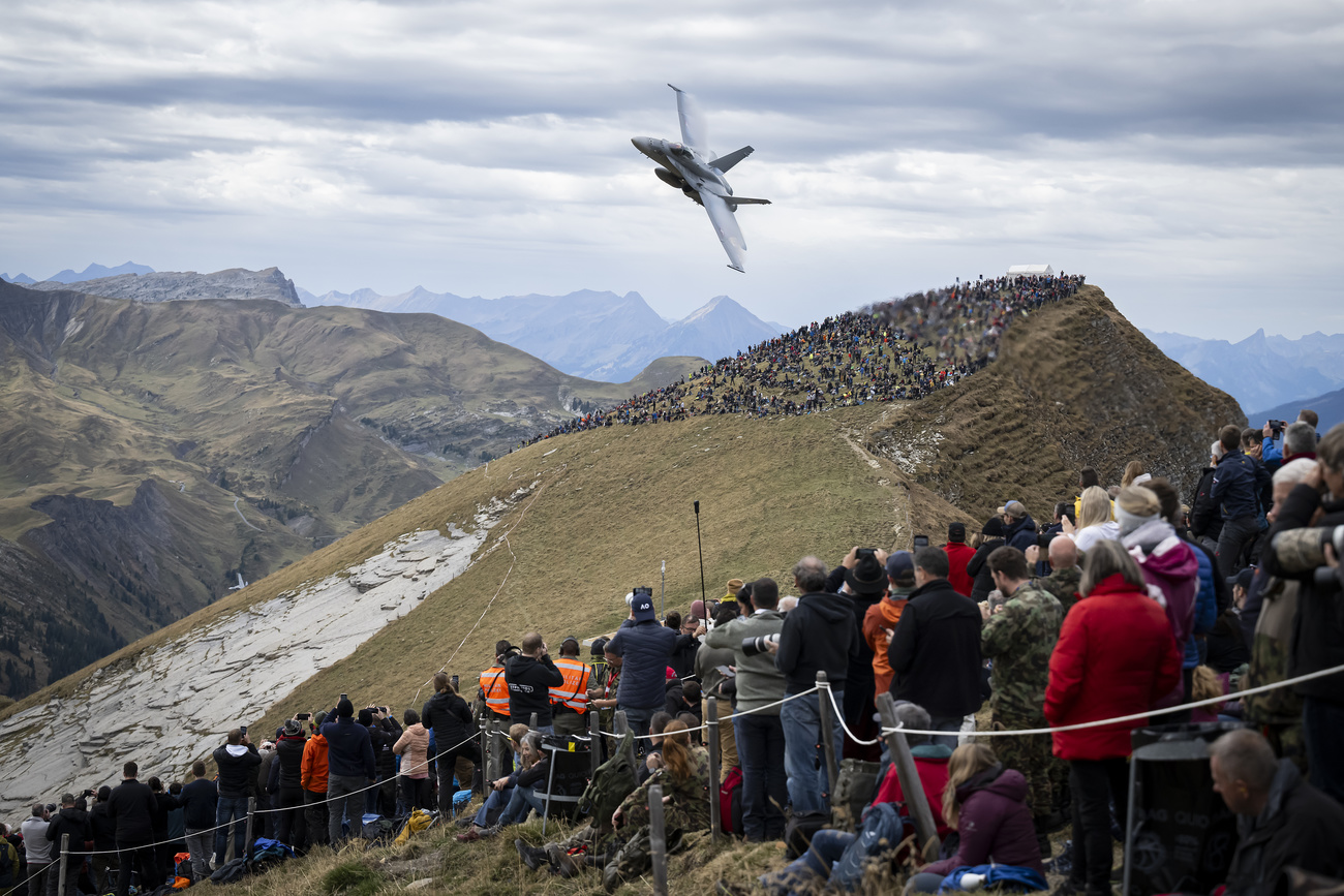 Kampfjet fliegt über Menschen, die an einem Berghang stehen